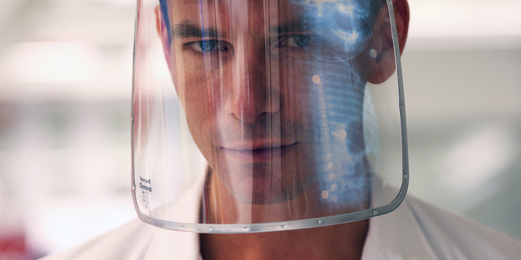 Portrait of a man in a transparent face shield in which an X-ray image is reflected.